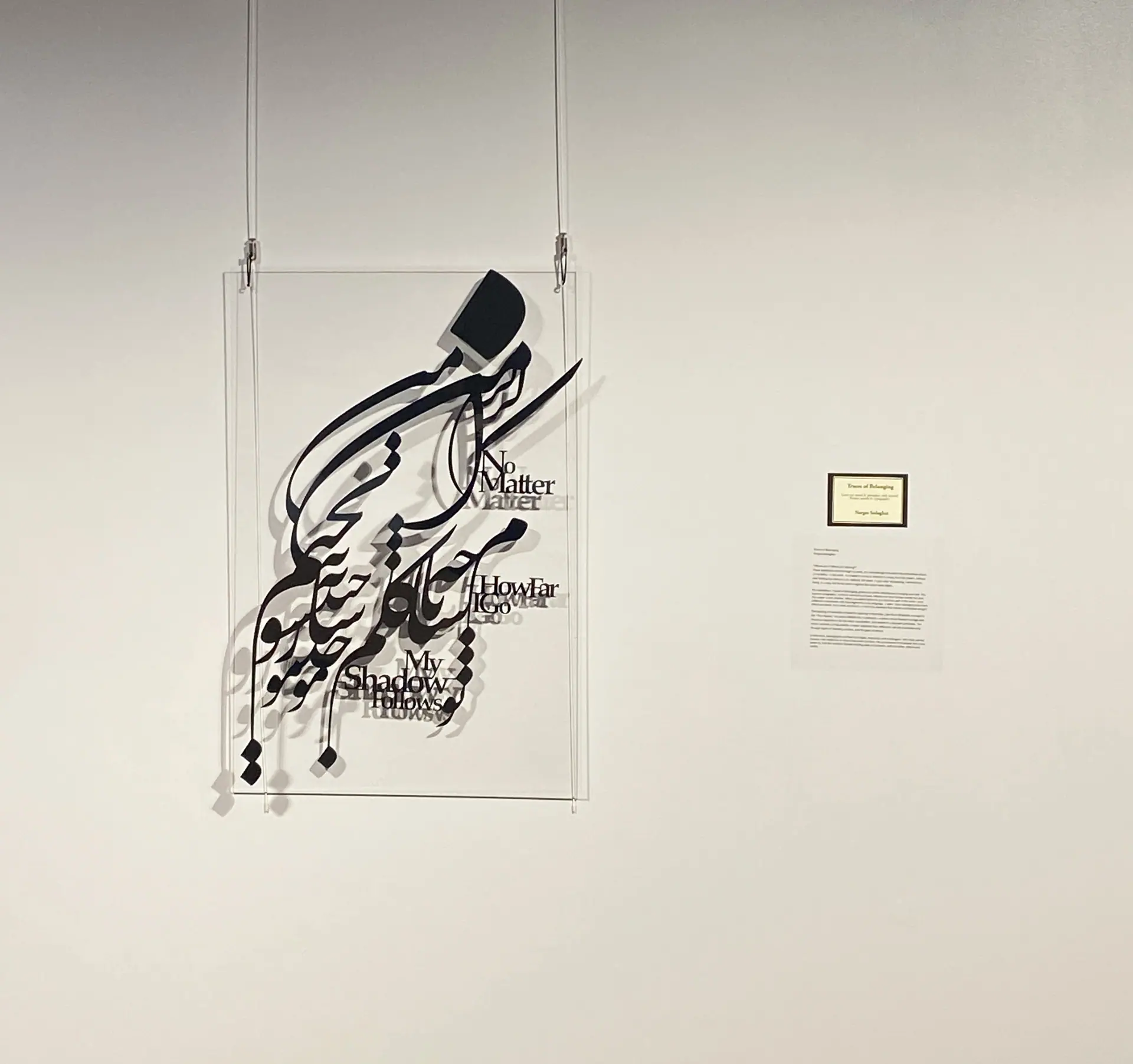 The calligraphy piece hanging on clear wires beside its wall label, without projection