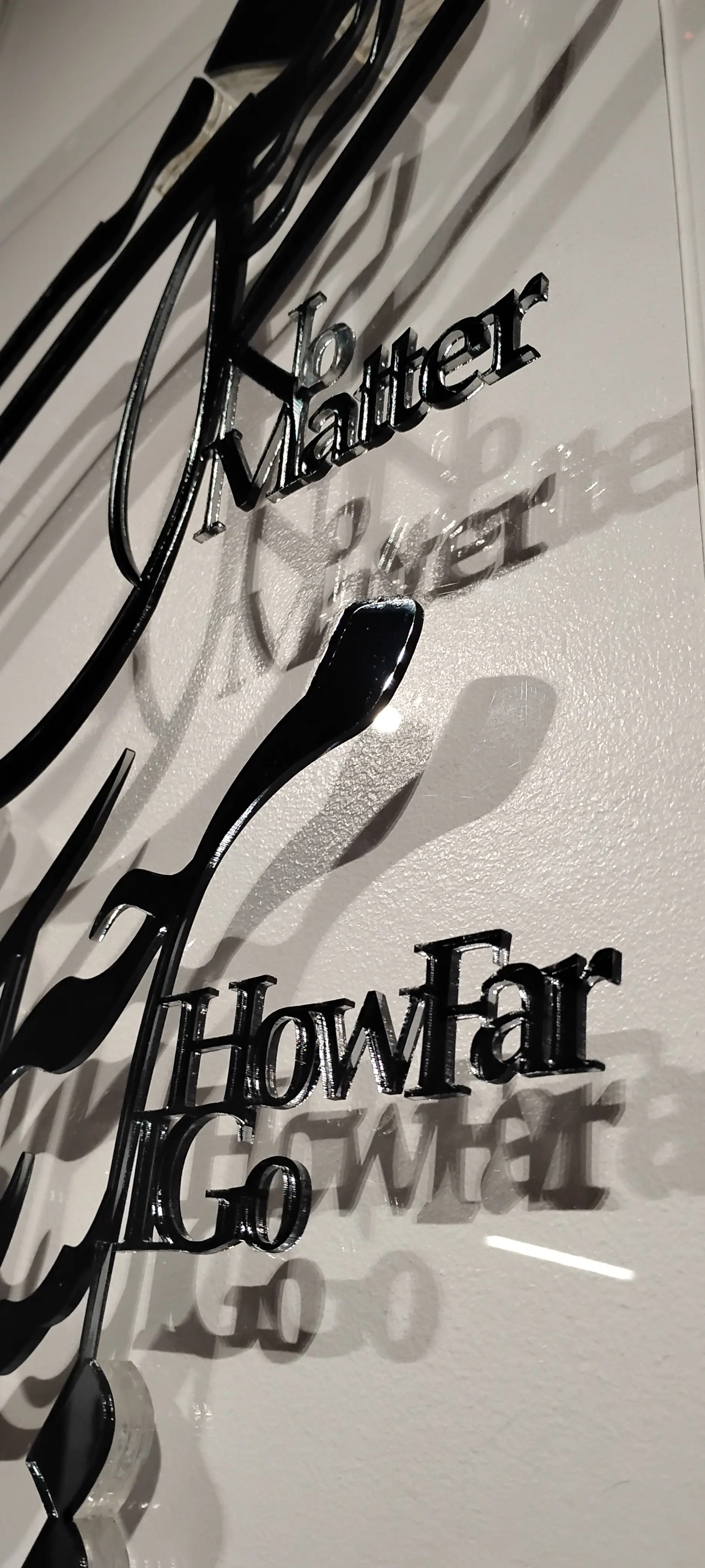 Detail: 'No Matter How Far I Go' in cut black letters, with its shadow on the wall