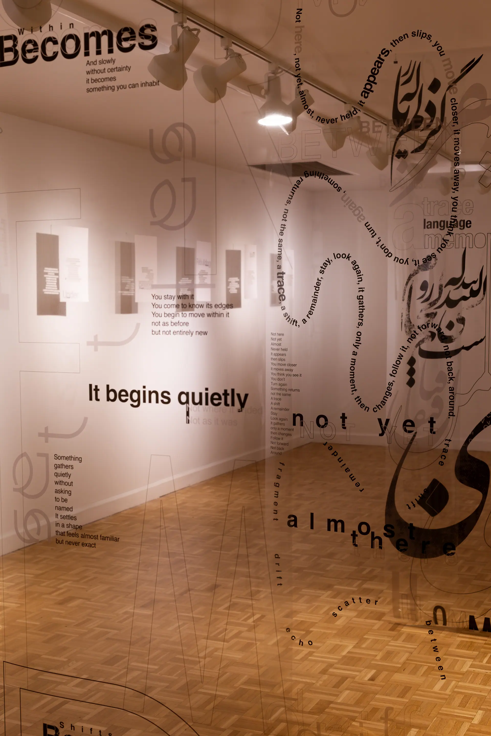 Looking through suspended transparent sheets of type toward the gallery wall