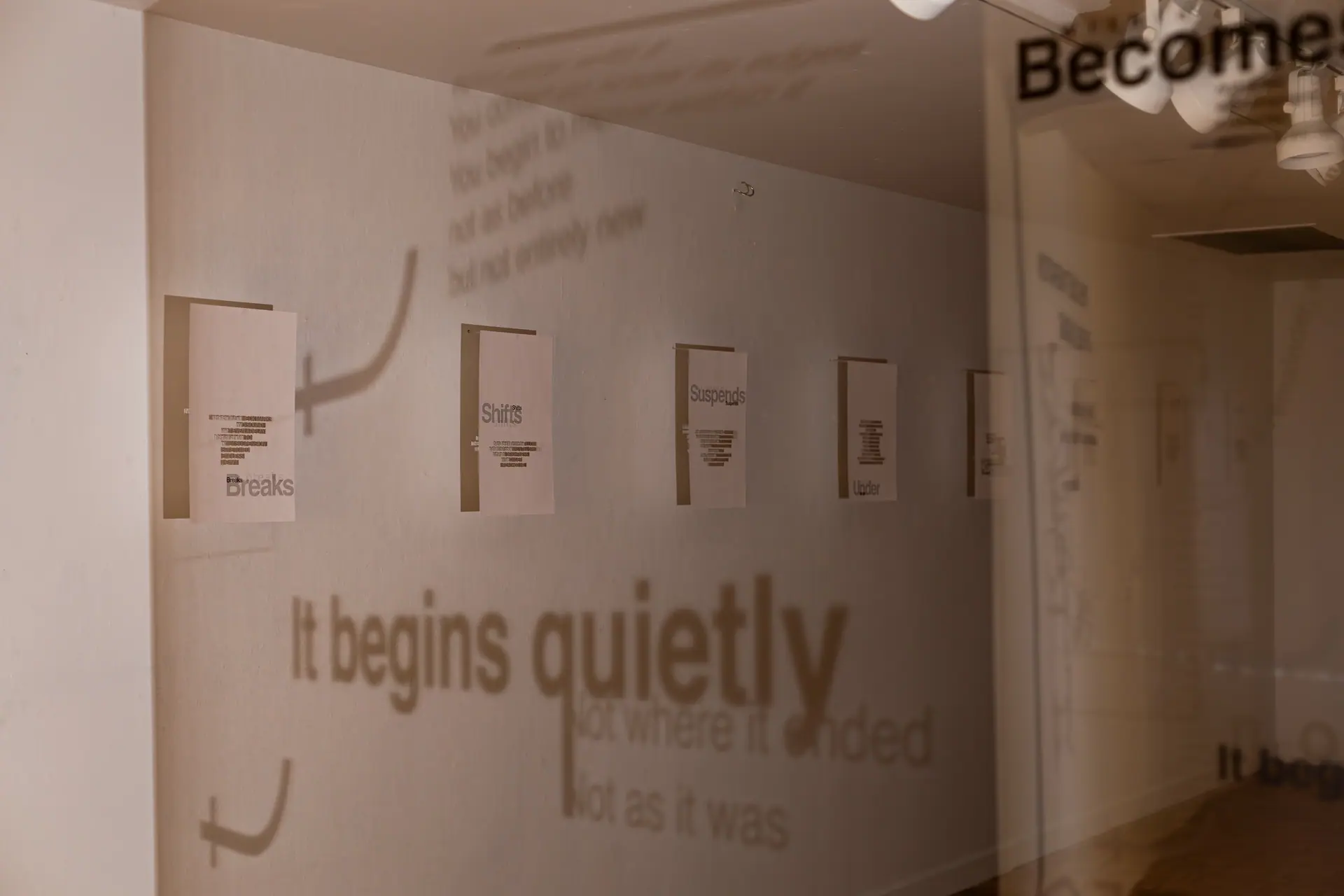 The shadow of 'It begins quietly' falls across a wall of hanging text panels