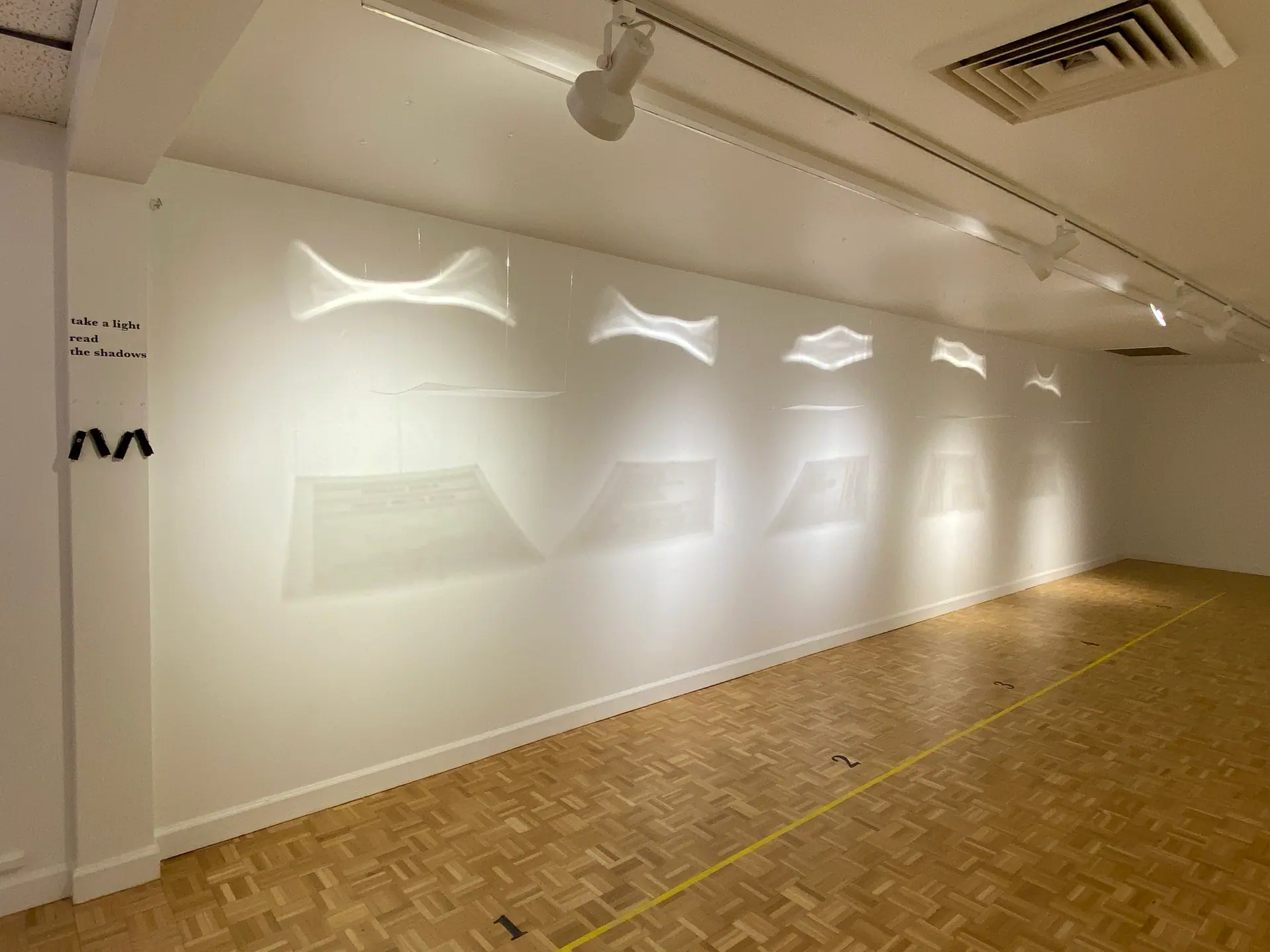 Gallery view: translucent text sheets hang along a white wall, casting wave-like light onto it