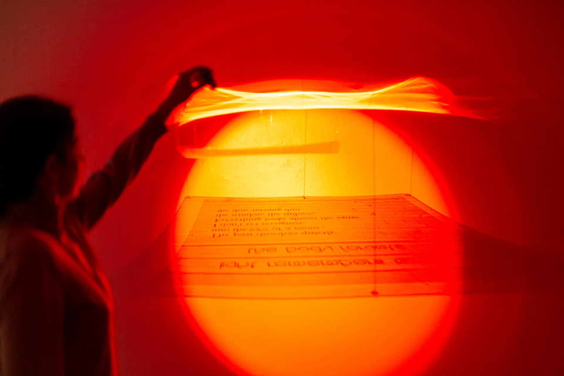 A hand lifts a suspended text sheet in front of a red and amber pool of light