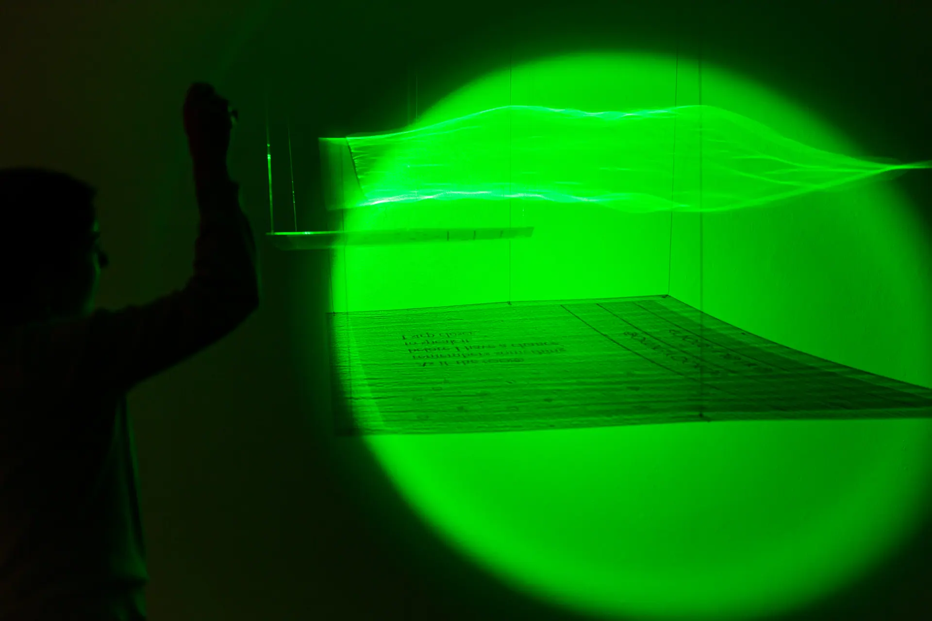 A visitor reaches toward a text sheet lit by a green circle of light