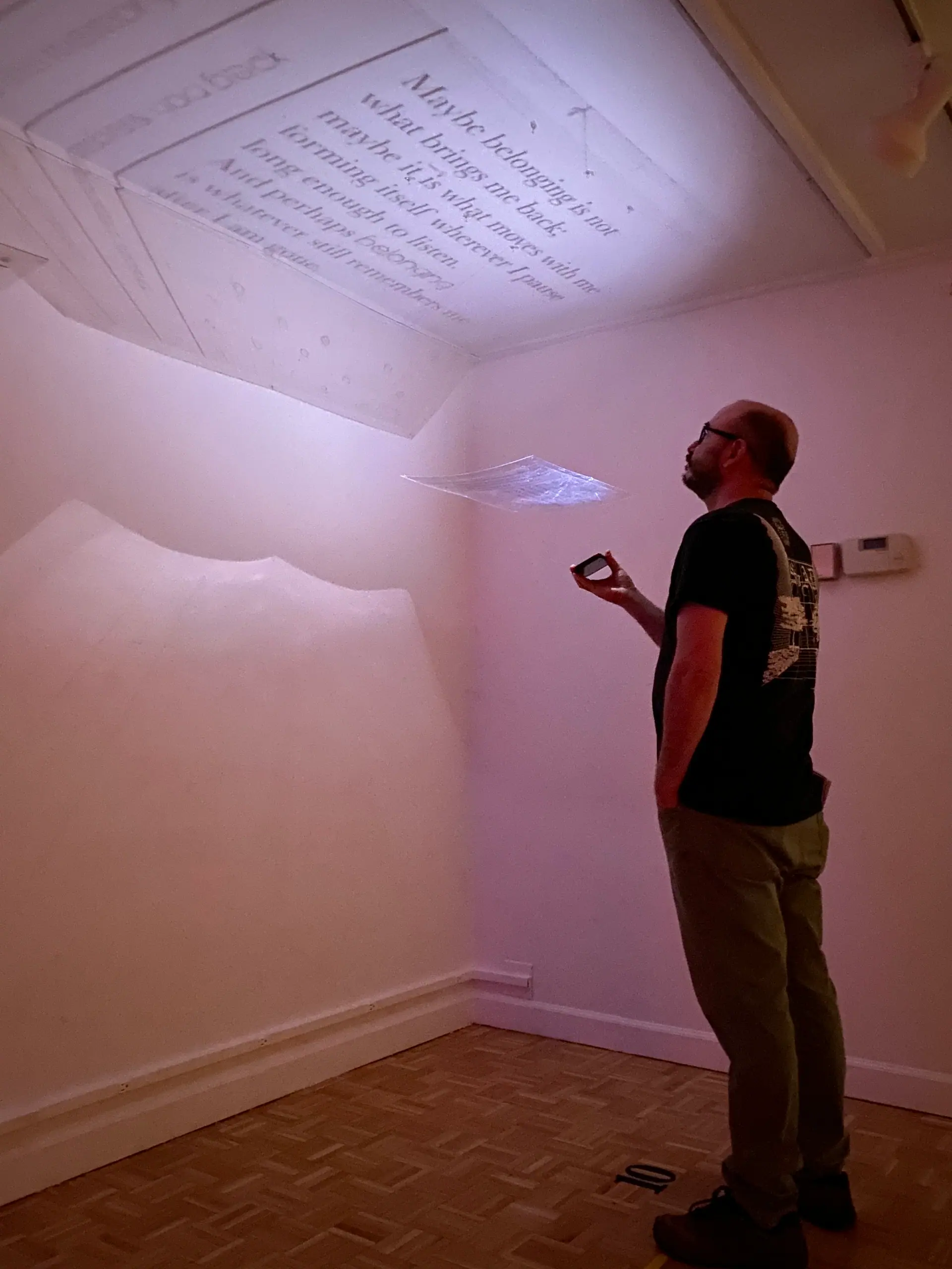 A visitor holding a phone light looks up at text reflected onto the ceiling