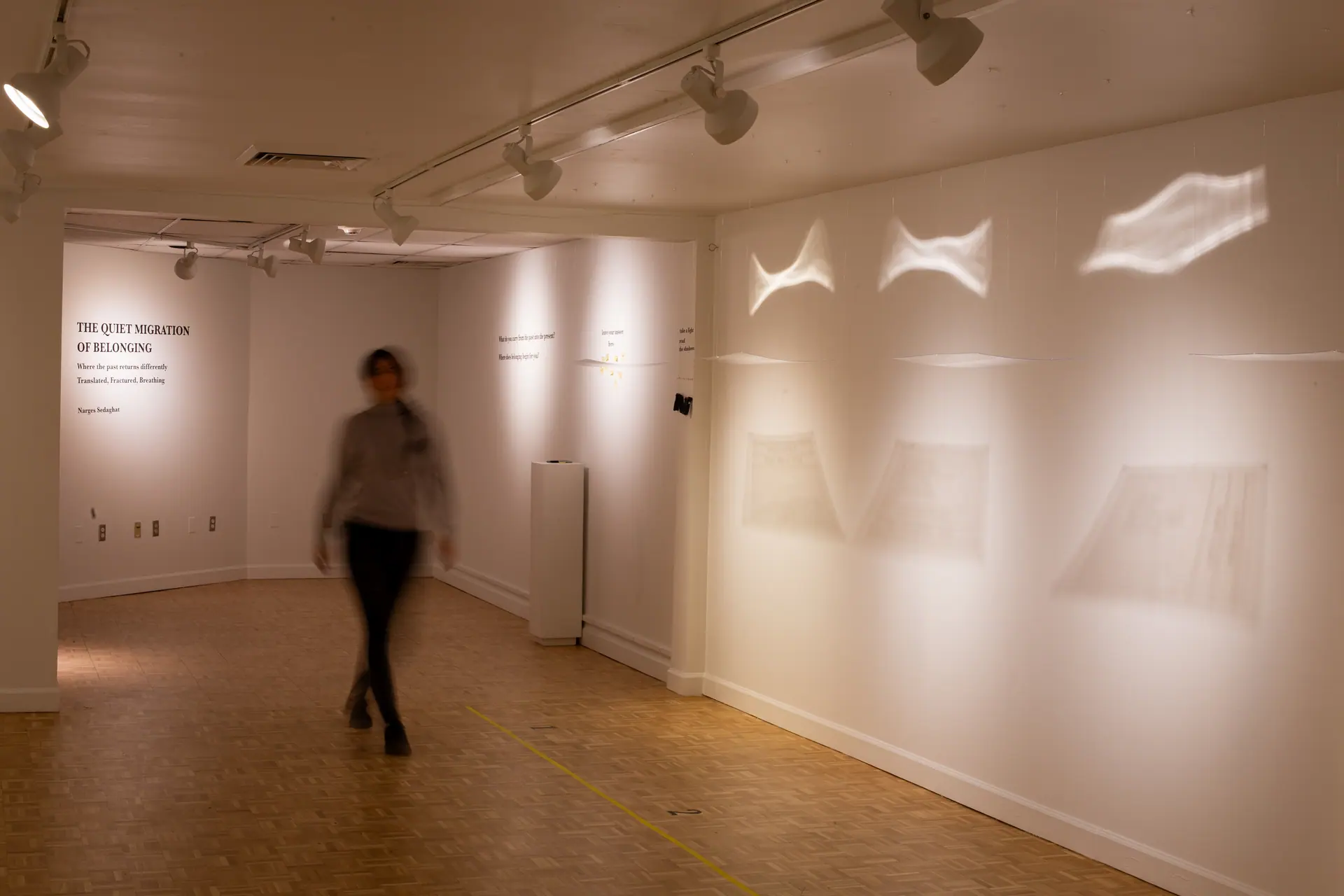 A figure walks through the gallery past the title wall and the hanging text sheets