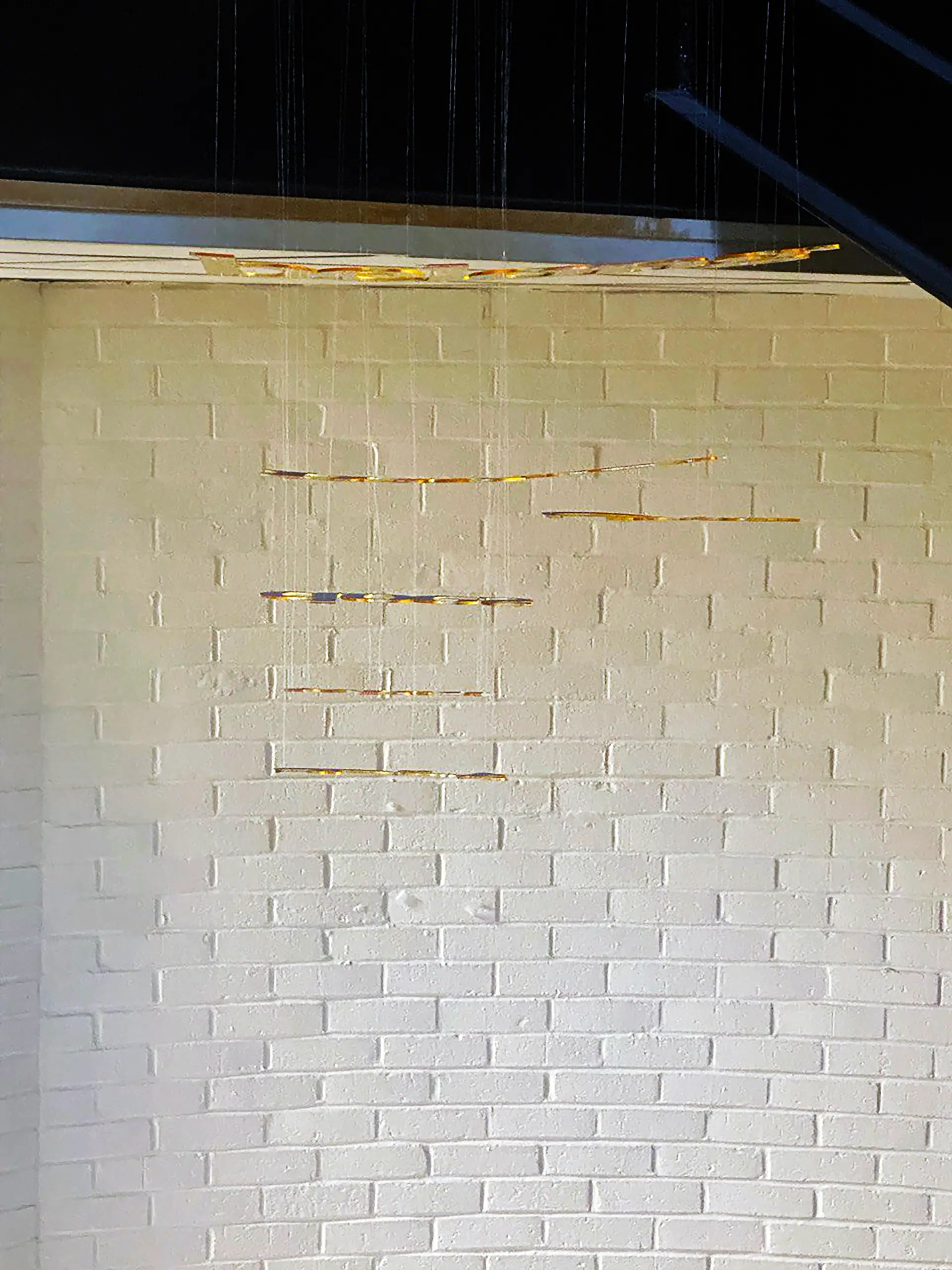 Suspended gold words seen face-on against the white brick wall of the stairwell